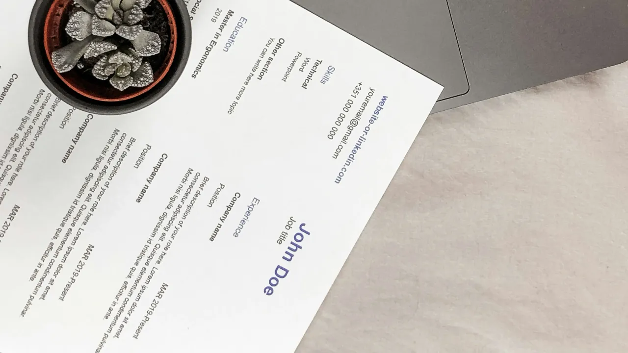 A printed resume on a laptop next to a plant